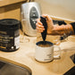 Handheld milk frother blending collagen powder into coffee beside Warrior Strong Wellness Collagen Peptides & Bone Broth, demonstrating easy mixing for drinks and recipes.