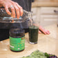 Person mixing Warrior Strong Wellness Organic Superfood Greens with water beside fresh produce for daily energy, digestion, detoxification, and immune support.